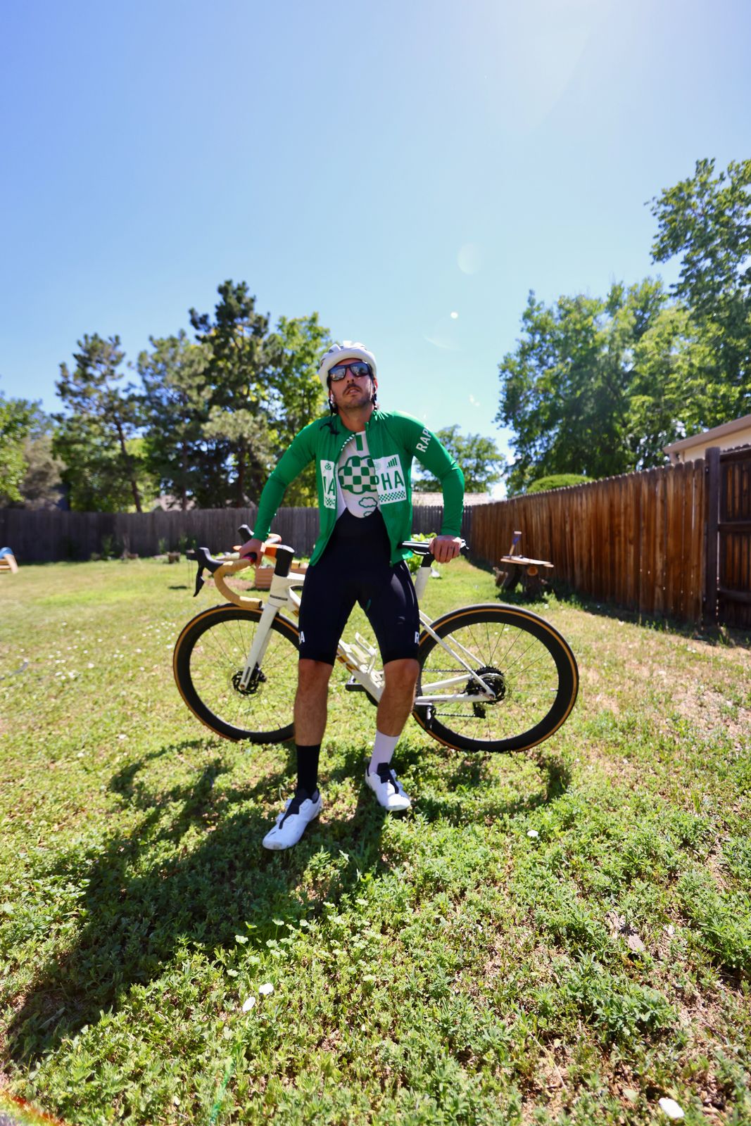 Carter Luense in green Rapha kit holding the white Trek behind him, backyard, Westminster