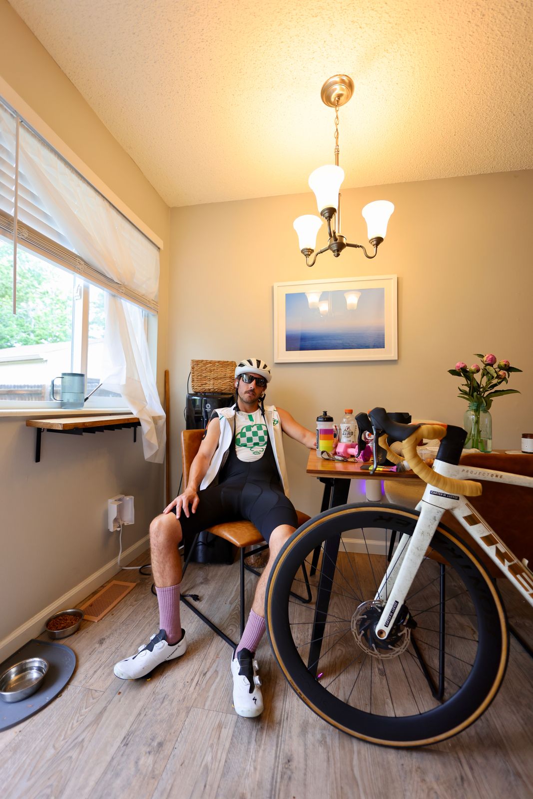 Carter Luense post-ride at the kitchen table in full kit, bottles out, the white Trek in the foreground